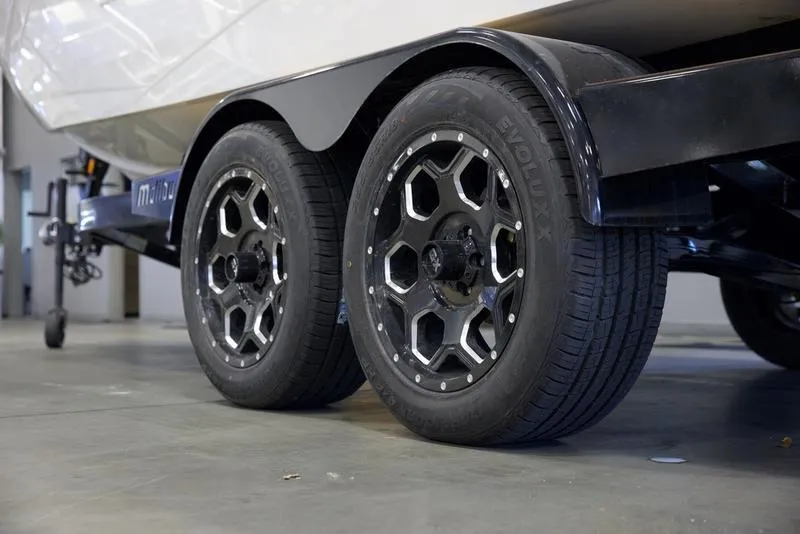 Slide: The Image of 2025 Malibu 23 LSV boat trailer with dual black wheels in a garage. - 6