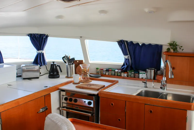 Slide: The Image of Interior of 2002 Lagoon 410 catamaran kitchen with wooden cabinets and ocean view. - 10