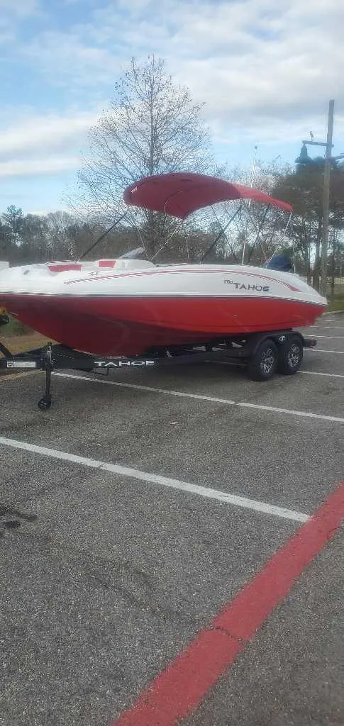 The Image of 2025 Tahoe 2150 boat with red canopy on trailer, parked outdoors under cloudy sky. - 0