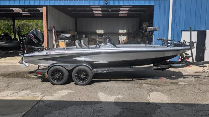 The Image of 2025 Triton 21XP Patriot boat on trailer, parked outside a blue garage. - 0