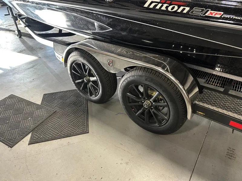 Slide: The Image of 2025 Triton 21XP Patriot boat trailer with black wheels in a garage setting. - 12