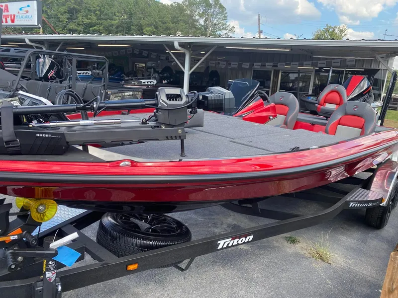 Slide: The Image of 2025 Triton 21XP Patriot boat in showroom, featuring red and gray seating, on a trailer. - 2