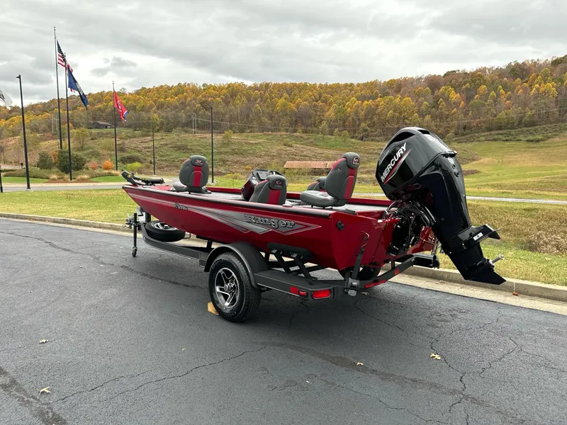 Slide: The Image of 2025 Ranger RT178C boat, red, parked on asphalt, scenic background with flags and autumn trees. - 2