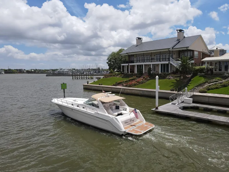 Slide: The Image of 1996 Sea Ray 500 Sundancer yacht cruising near a waterfront house under a cloudy sky. - 12