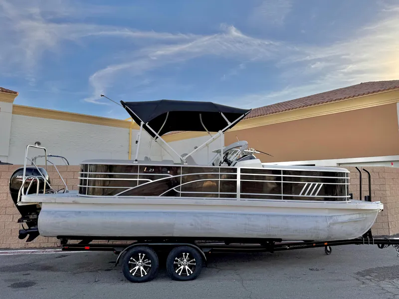 The Image of 2021 Bennington 23 LPD pontoon boat on trailer, parked outdoors under blue sky. - 0