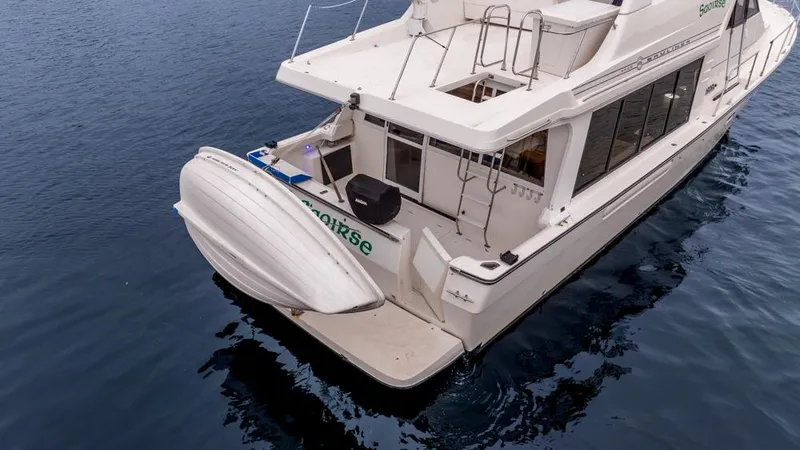 Slide: The Image of Bayliner 4788 Pilot House Motoryacht 2000 on calm water, rear view with attached dinghy. - 8