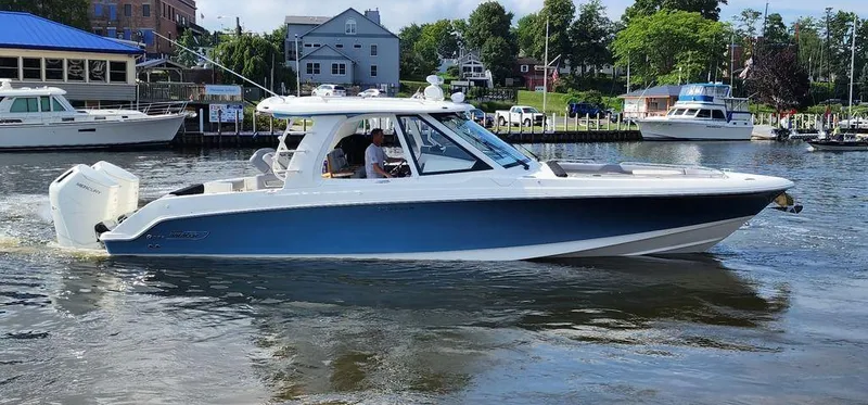Slide: The Image of 2025 Boston Whaler 380 Realm cruising on a calm river near a marina. - 0