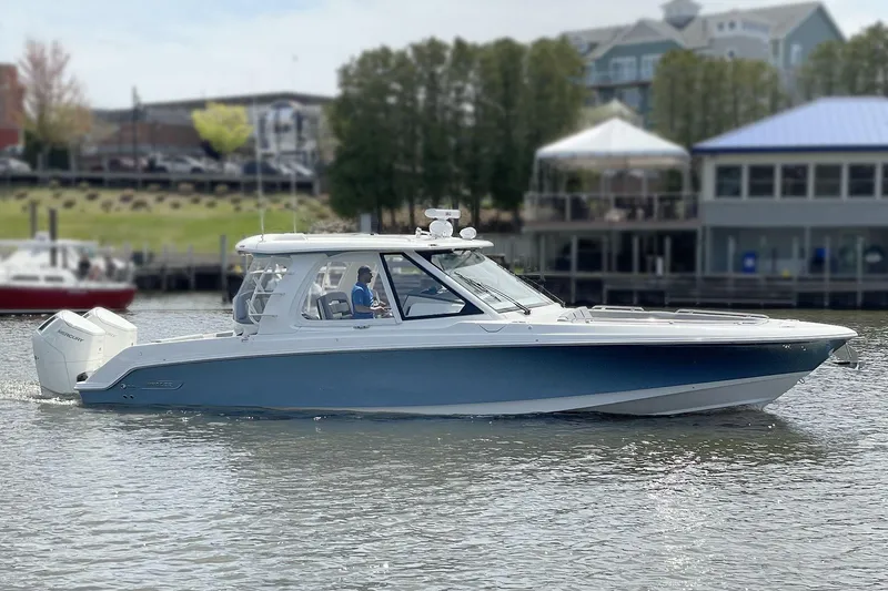 Slide: The Image of 2025 Boston Whaler 380 Realm boat cruising on a calm waterfront near buildings. - 1