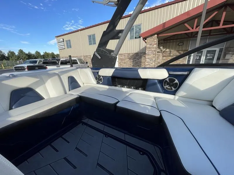 Slide: The Image of 2017 Malibu 21 VLX boat interior with white and navy seating, near a building. - 30