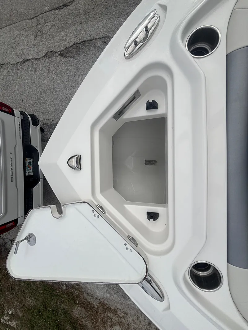 Slide: The Image of 2025 Sailfish 232 CC boat storage compartment, open lid, white interior, next to a vehicle. - 20