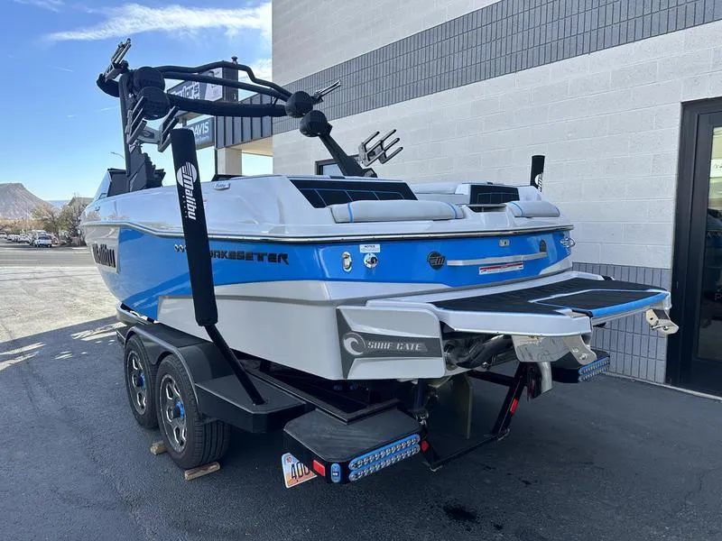 Slide: The Image of 2023 Malibu 23 LSV boat on trailer, blue and white design, parked outside a building. - 5