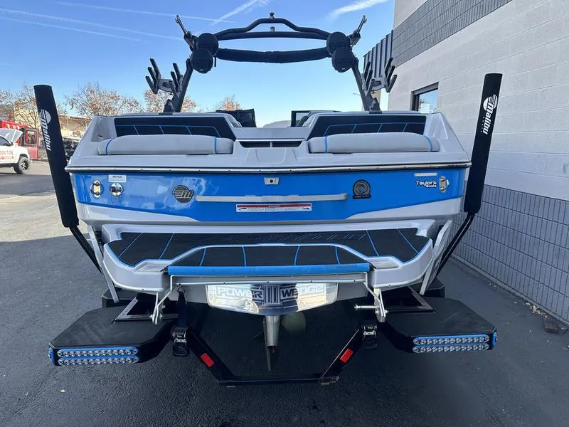 Slide: The Image of 2023 Malibu 23 LSV boat rear view with blue and white design, parked outdoors. - 6