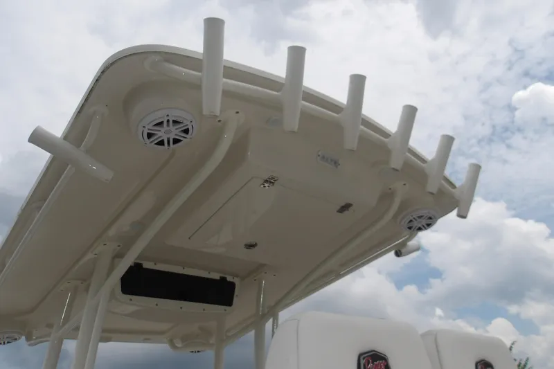 Slide: The Image of 2025 Ranger 2600 Bay boat T-top with rod holders and speakers against cloudy sky. - 13