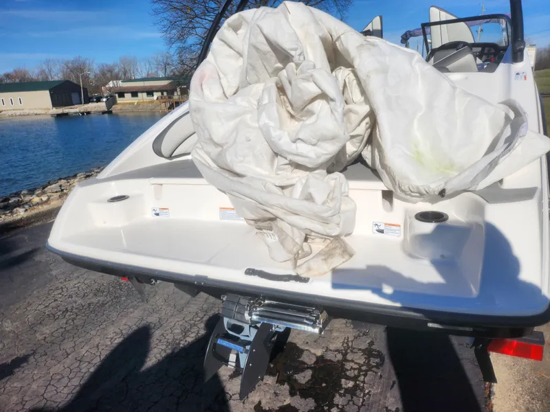 Slide: The Image of 2023 Yamaha Boats AR190 with tarp, parked near a lake. - 2
