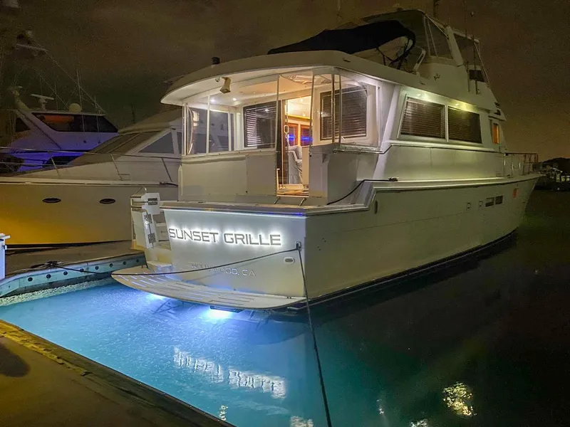 Slide: The Image of 1990 Hatteras 62 Cockpit Motor Yacht docked at night with illuminated name "Sunset Grille". - 3