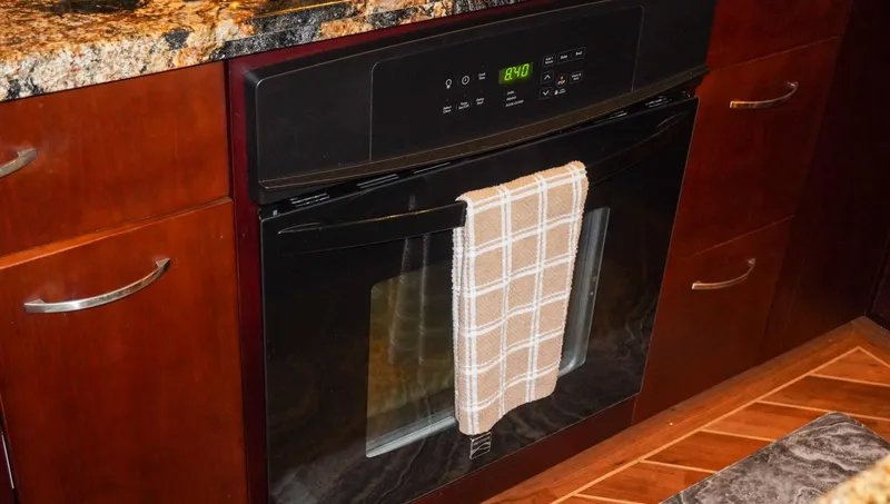 Slide: The Image of Modern kitchen oven with a plaid towel, granite countertop, and wooden cabinetry on a 1990 Hatteras yacht. - 43