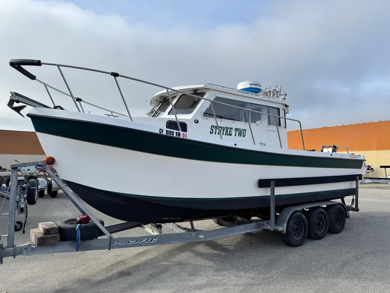 Slide: The Image of 1999 Osprey 26 Legend boat on trailer, named "Stryke Two," parked outdoors. - 0