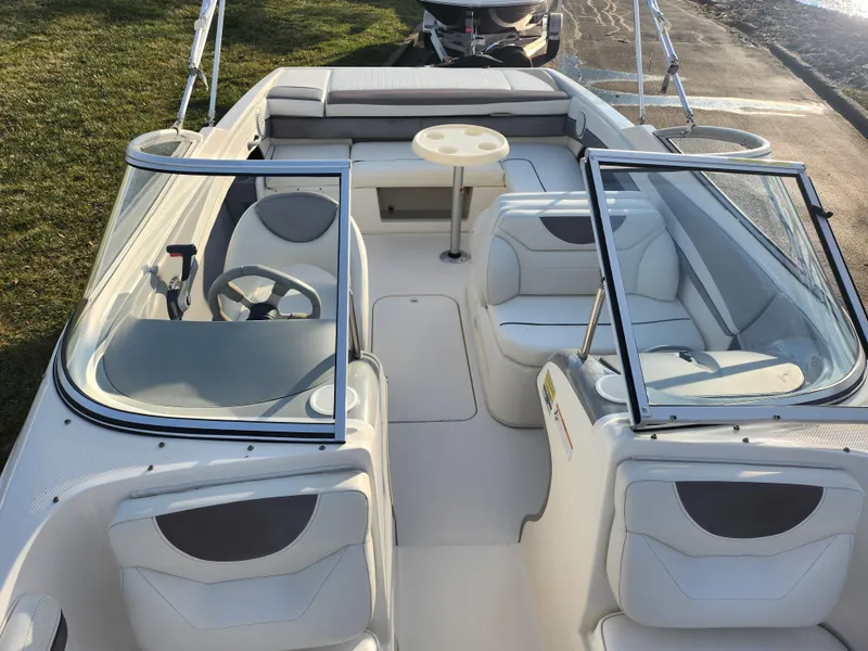 Slide: The Image of 2007 Bayliner 225 boat interior with seating and table, docked near grassy area. - 19