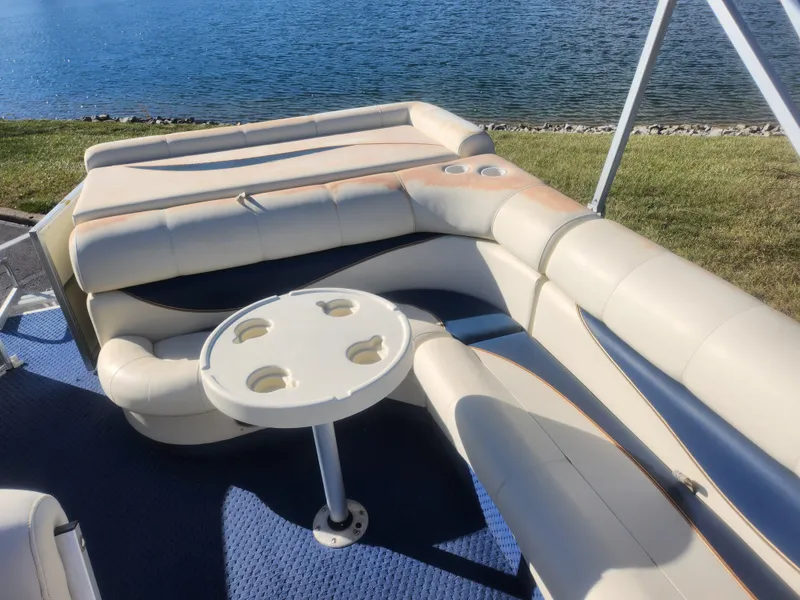 Slide: The Image of 2005 Odyssey 522C boat interior with beige seating and cupholder table by the water. - 14