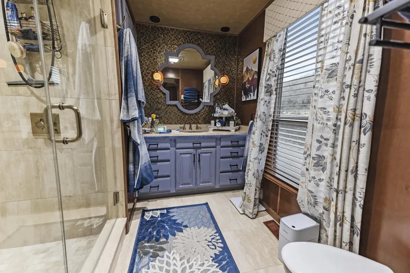 Slide: The Image of Modern bathroom with glass shower, blue vanity, decorative mirror, and floral rug. - 24