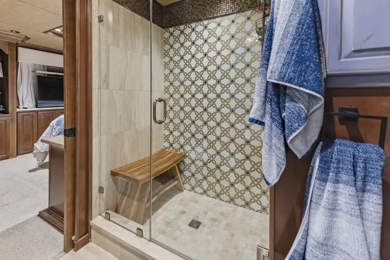 Slide: The Image of Luxurious shower with glass door, wooden bench, and patterned tile wall in a modern bathroom. - 25