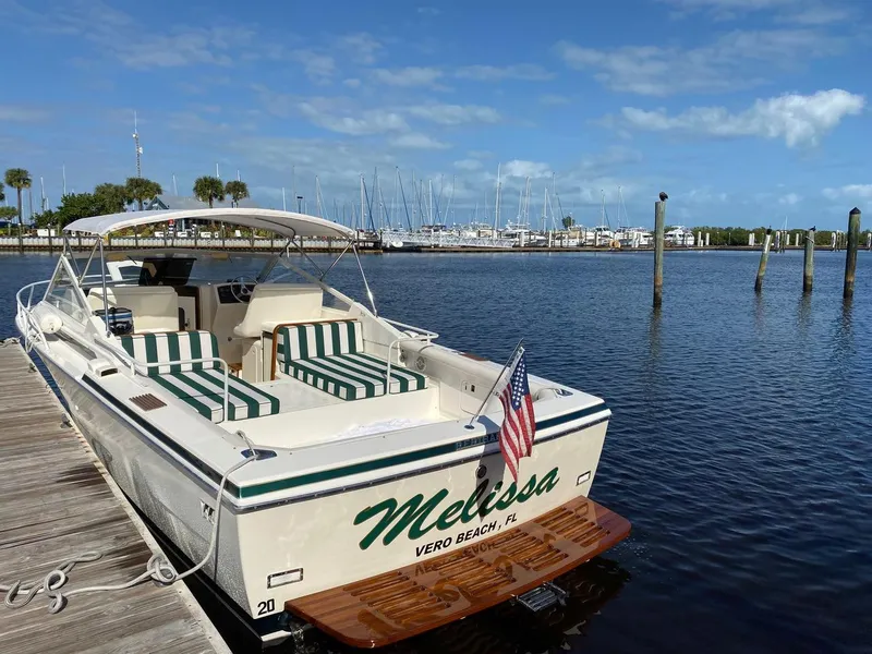 Slide: The Image of 1988 Bertram 28 Moppie boat docked, featuring striped seating and American flag, Vero Beach. - 0