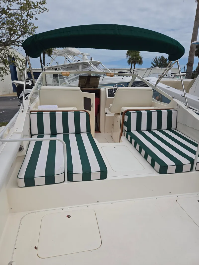Slide: The Image of 1988 Bertram 28 Moppie boat with green-striped seating and canopy, docked outdoors. - 25