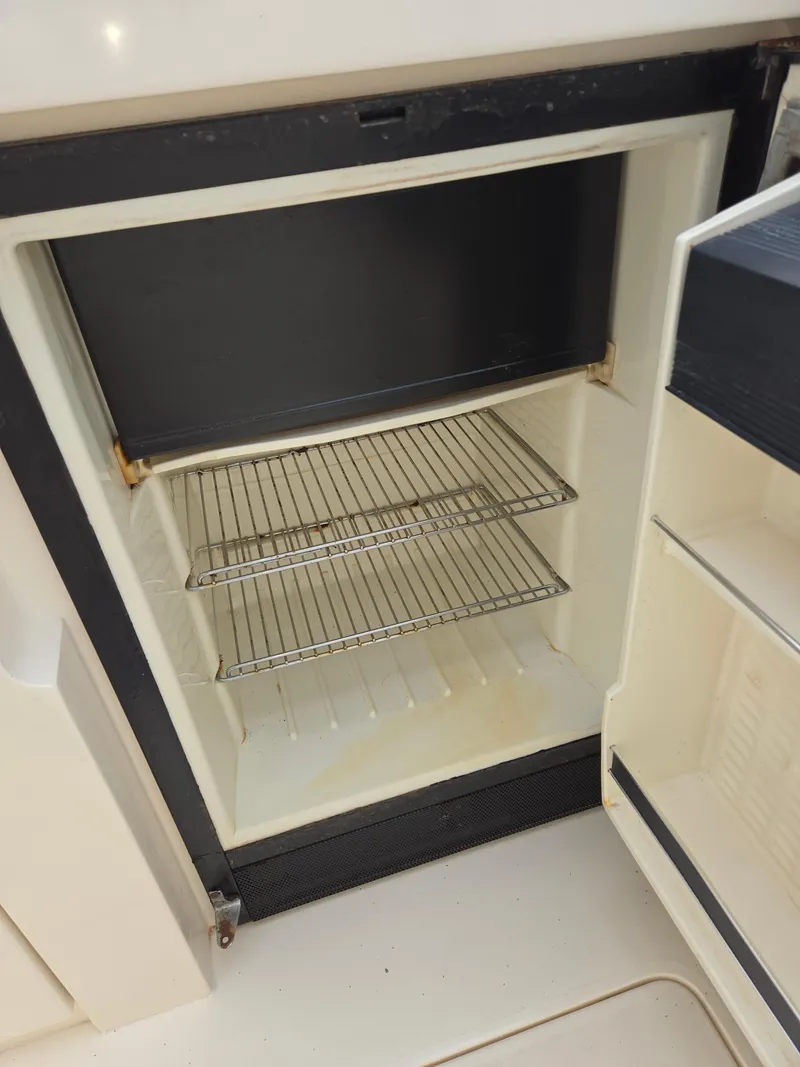 Slide: The Image of Empty refrigerator inside a 1988 Bertram 28 Moppie boat, featuring wire shelves. - 28