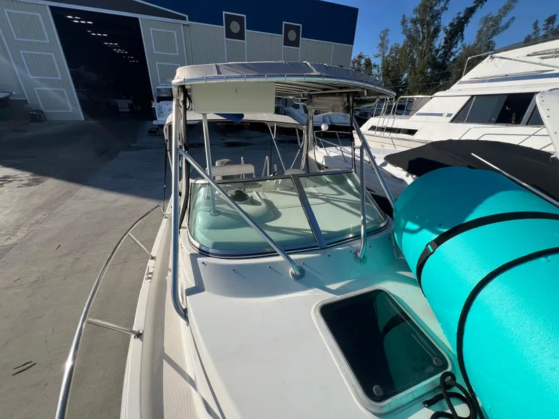 Slide: The Image of 2000 Robalo 2440 Walkaround boat with teal kayak on deck, docked near warehouse. - 14
