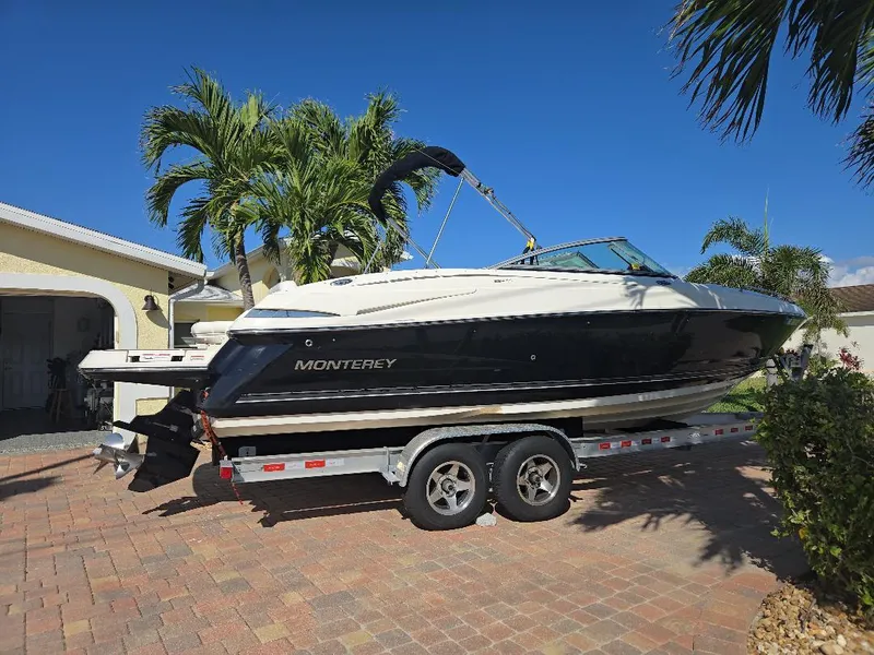 The Image of 2010 Monterey 254FS boat on trailer, parked in driveway with palm trees and clear blue sky. - 0