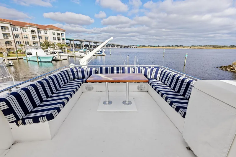 Slide: The Image of 1987 Hatteras 68 Cockpit Motor Yacht with striped seating and table, docked by waterfront. - 10