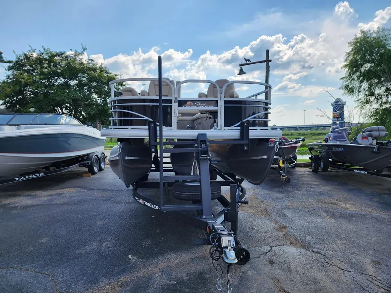 Slide: The Image of 2023 Sun Tracker SF24 pontoon boat on trailer, parked outdoors under a blue sky. - 11
