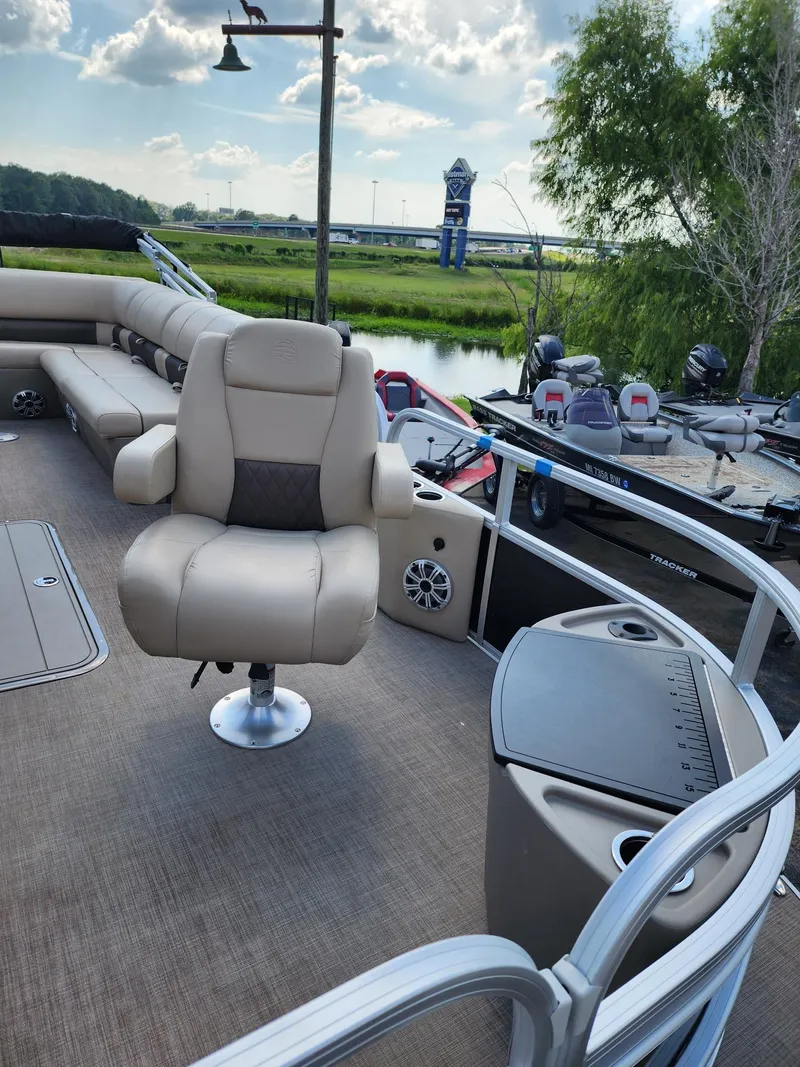 Slide: The Image of 2023 Sun Tracker SF24 pontoon boat interior with plush seating and scenic river backdrop. - 3