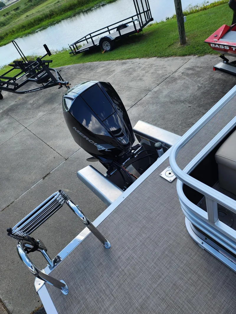 Slide: The Image of 2023 Sun Tracker SF24 pontoon boat with outboard motor, docked near a lake. - 4