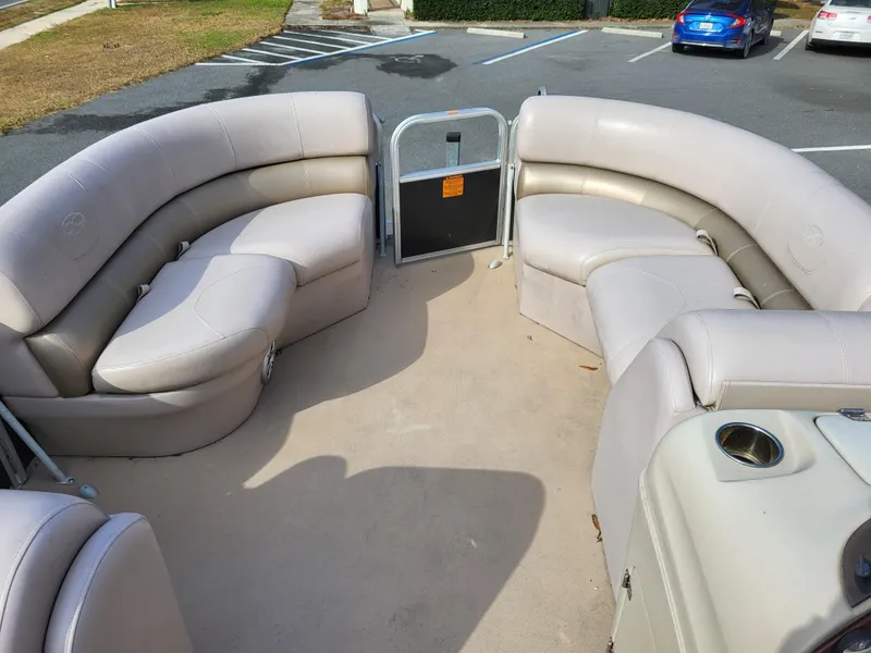 Slide: The Image of 2013 Xcursion X23RFC pontoon boat interior with beige seating in a parking lot. - 4