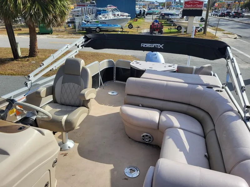 Slide: The Image of 2013 Xcursion X23RFC pontoon boat with beige seating and helm, parked outdoors. - 5