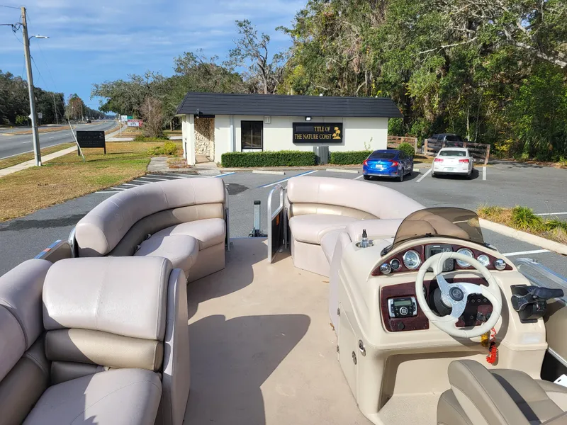 Slide: The Image of 2013 Xcursion X23RFC pontoon boat with beige seating and steering console, parked near a small building. - 7