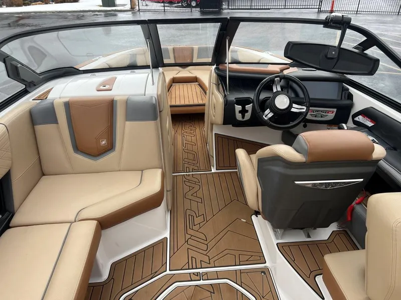Slide: The Image of 2019 Nautique G25 boat interior with tan and brown seating, modern dashboard, and wood-style flooring. - 14