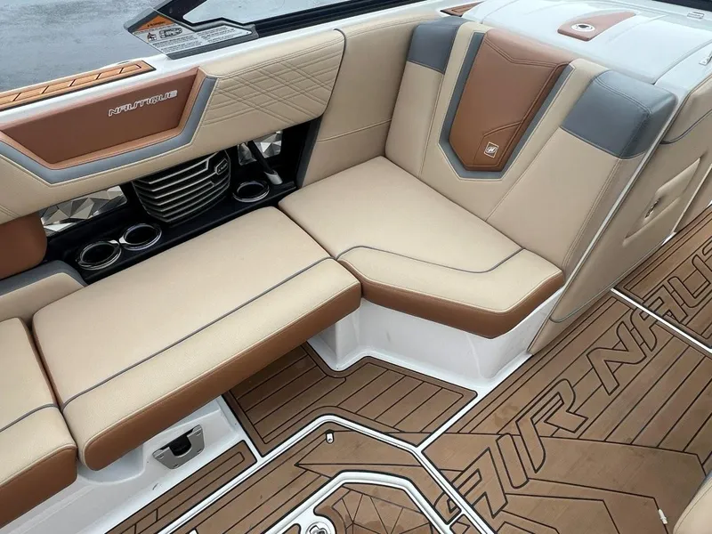 Slide: The Image of 2019 Nautique G25 boat interior with tan and brown seating, cup holders, and branded flooring. - 16