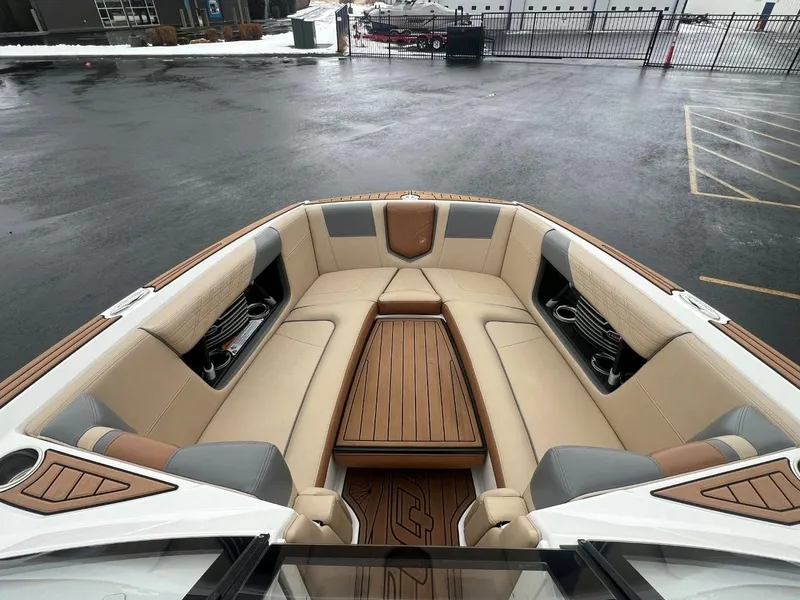 Slide: The Image of 2019 Nautique G25 boat interior with beige seating and wooden accents, parked on wet pavement. - 21