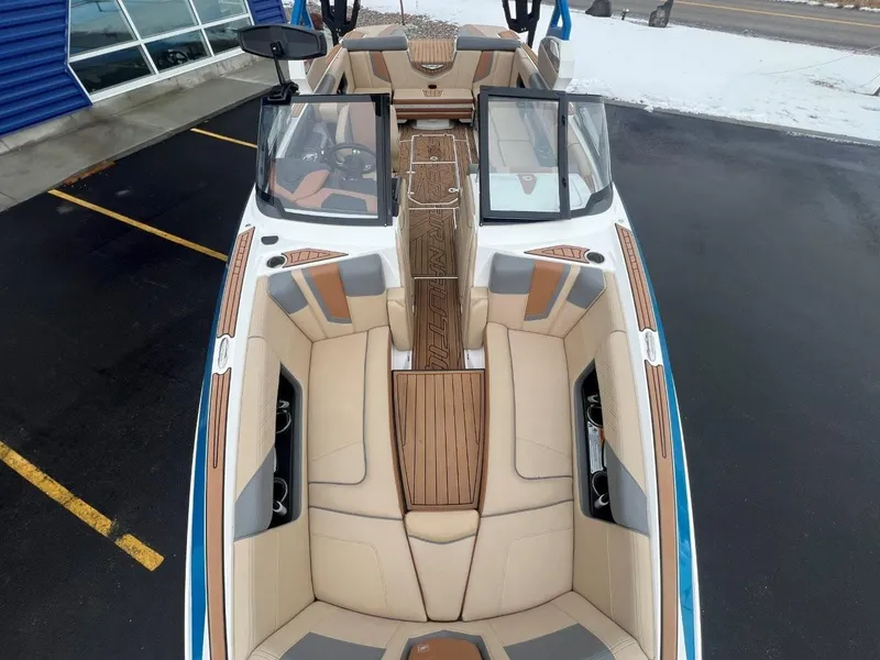 Slide: The Image of 2019 Nautique G25 boat interior with beige seating and wood accents, parked near a building. - 22