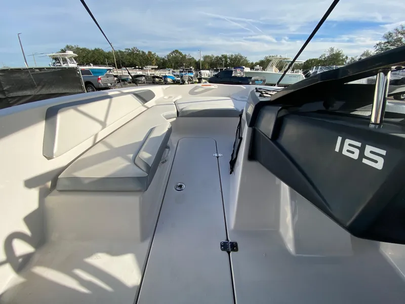 Slide: The Image of 2018 Scarab 165 G boat interior with seating and dashboard in a marina setting. - 10