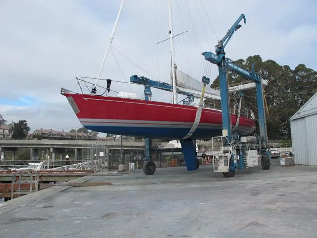 Slide: The Image of Red 1985 Santa Cruz 70 sailboat lifted by crane at marina dock. - 49