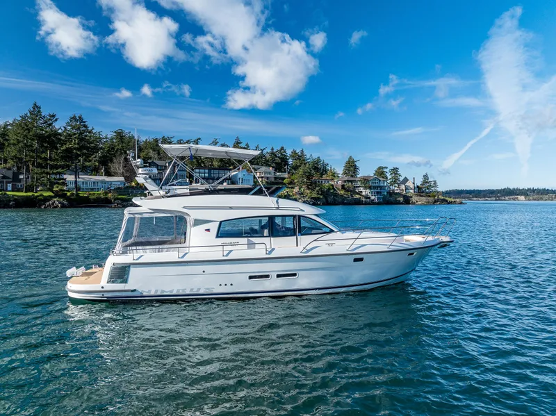 Slide: The Image of 2024 Nimbus 405 Flybridge yacht cruising on a scenic lake under a clear blue sky. - 1