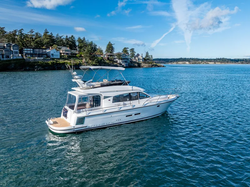 Slide: The Image of 2024 Nimbus 405 Flybridge yacht cruising on a scenic blue lake near a forested shoreline. - 25