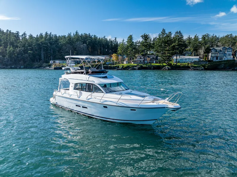 Slide: The Image of 2024 Nimbus 405 Flybridge yacht cruising on a scenic lake with forested shoreline. - 26