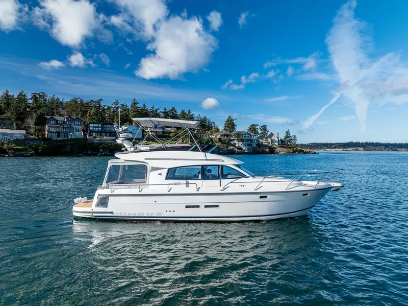 Slide: The Image of 2024 Nimbus 405 Flybridge yacht cruising on a serene lake under a clear blue sky. - 29