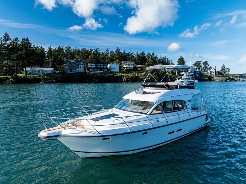 Slide: The Image of 2024 Nimbus 405 Flybridge yacht cruising on a scenic lake with houses and trees in the background. - 33