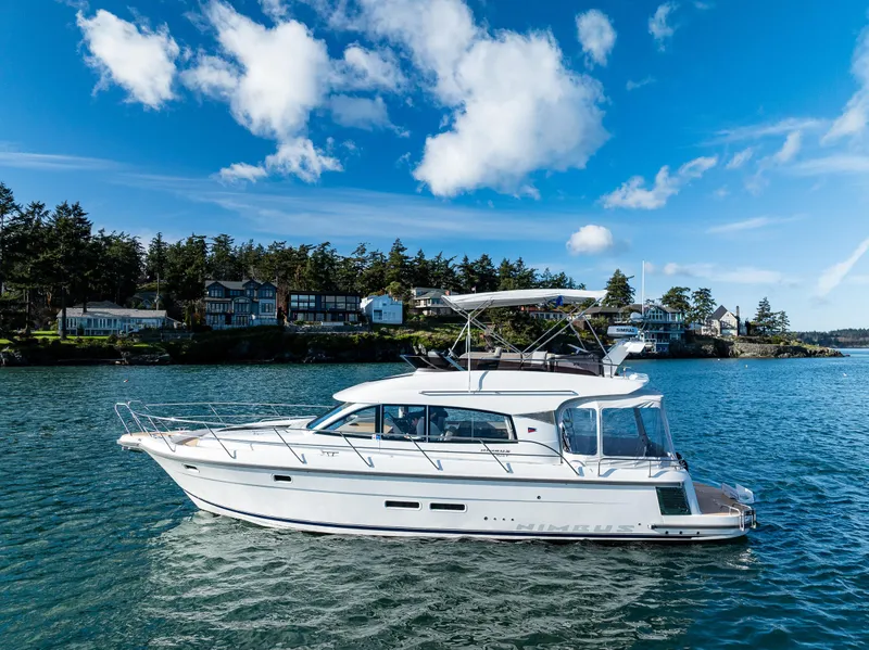 Slide: The Image of 2024 Nimbus 405 Flybridge yacht cruising on a scenic lake under a clear blue sky. - 34