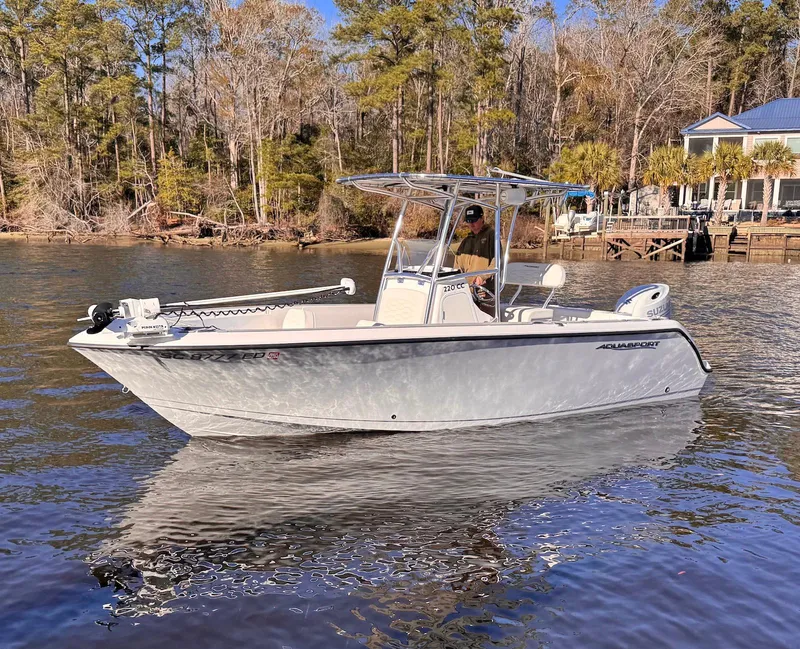 Slide: The Image of 2024 Aquasport 2200 Center Console boat on a calm river near a wooded shoreline. - 2